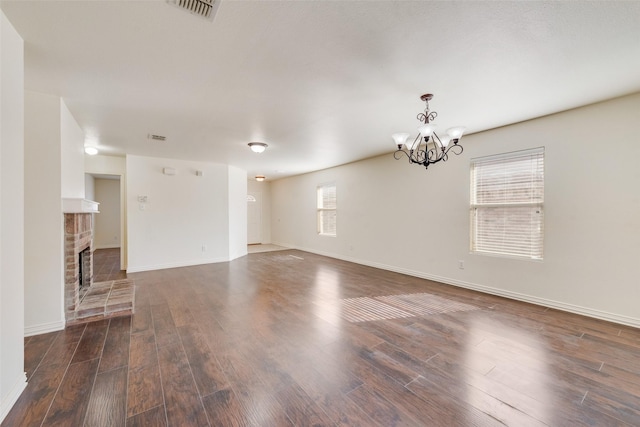 unfurnished living room with dark wood-type flooring, a brick fireplace, and a notable chandelier