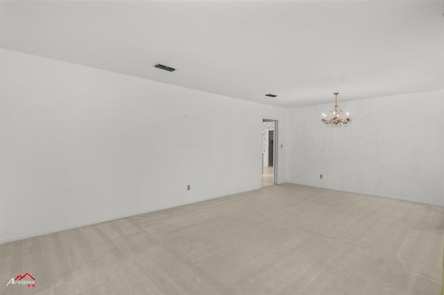 spare room featuring light colored carpet and an inviting chandelier