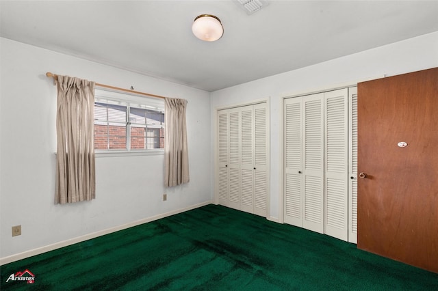 unfurnished bedroom featuring two closets and dark colored carpet