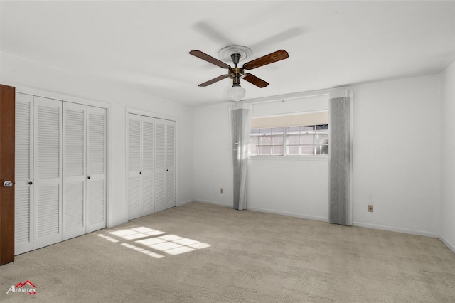 unfurnished bedroom featuring ceiling fan, light colored carpet, and multiple closets