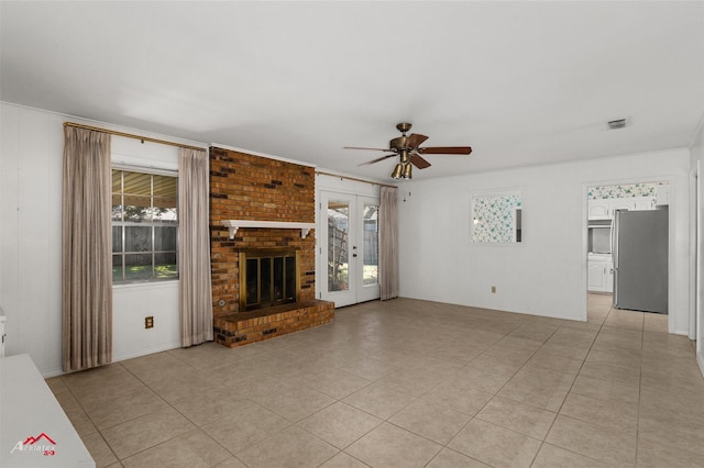 unfurnished living room with ceiling fan, light tile patterned flooring, french doors, and a brick fireplace