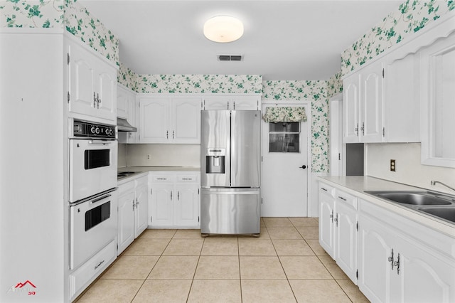 kitchen featuring stainless steel refrigerator with ice dispenser, white cabinetry, and white double oven