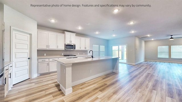 kitchen featuring ceiling fan, sink, white cabinetry, and an island with sink