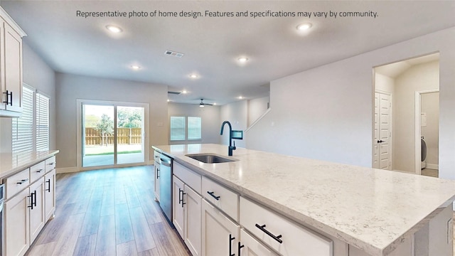 kitchen with stainless steel dishwasher, sink, white cabinetry, a kitchen island with sink, and light stone countertops