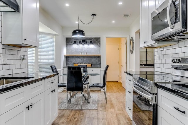 kitchen featuring pendant lighting, white cabinets, stainless steel appliances, backsplash, and light wood-type flooring