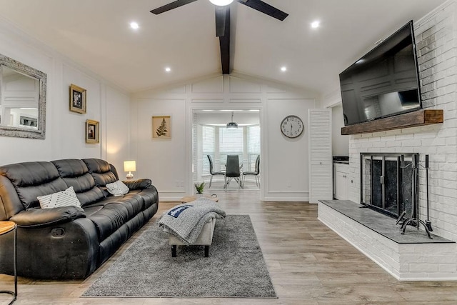 living room with ceiling fan, vaulted ceiling with beams, light wood-type flooring, and a fireplace