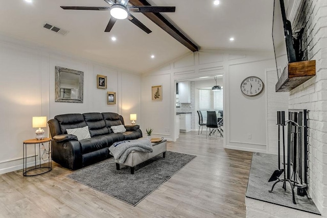 living room featuring a fireplace, ceiling fan, light hardwood / wood-style floors, and lofted ceiling with beams