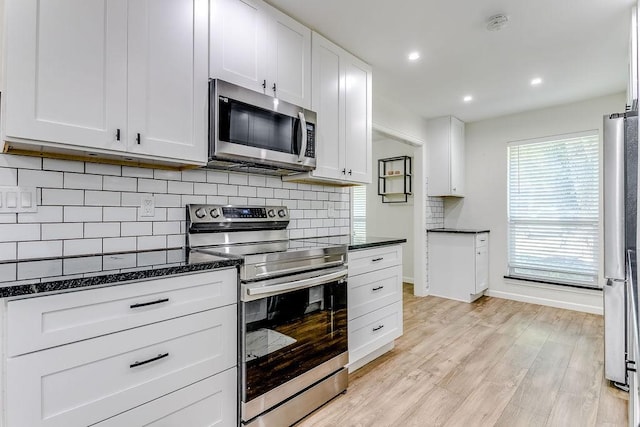 kitchen with appliances with stainless steel finishes, white cabinetry, dark stone counters, tasteful backsplash, and light hardwood / wood-style floors