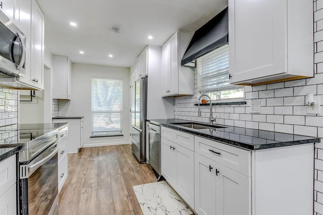 kitchen with white cabinetry, appliances with stainless steel finishes, dark stone countertops, light hardwood / wood-style flooring, and sink