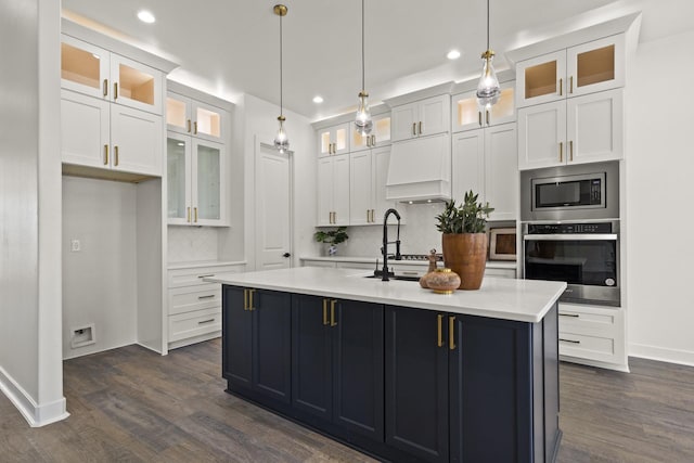 kitchen with appliances with stainless steel finishes, an island with sink, white cabinets, and decorative light fixtures