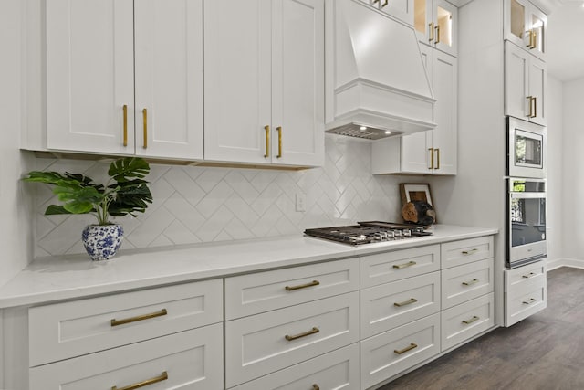 kitchen with tasteful backsplash, dark hardwood / wood-style floors, white cabinetry, appliances with stainless steel finishes, and custom range hood