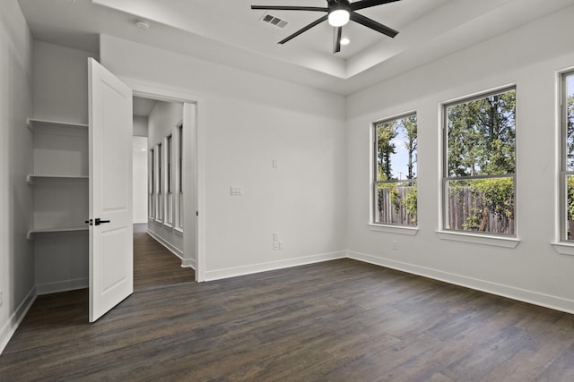 empty room featuring a raised ceiling, ceiling fan, and dark hardwood / wood-style flooring