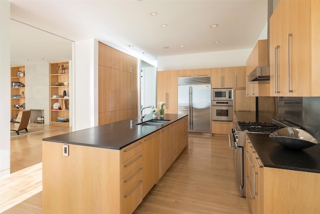 kitchen featuring light brown cabinets, sink, a center island with sink, and built in appliances