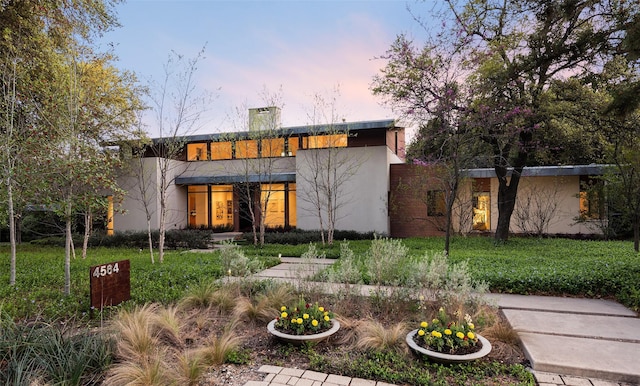 back house at dusk featuring a lawn