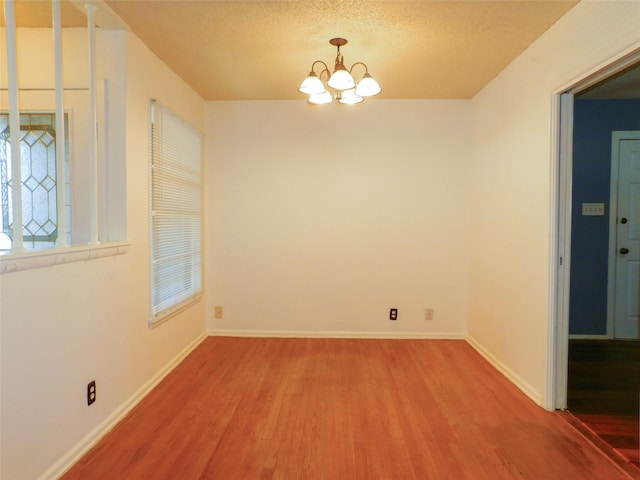 unfurnished dining area with a textured ceiling, a chandelier, and hardwood / wood-style floors