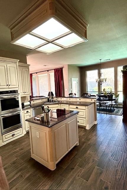 kitchen with dark wood-type flooring, a center island, kitchen peninsula, and an inviting chandelier