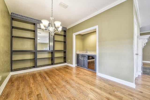 unfurnished dining area with crown molding, built in features, an inviting chandelier, wet bar, and light wood-type flooring