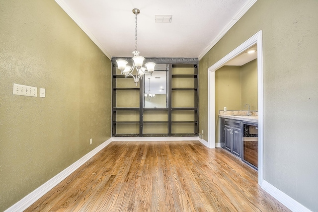 unfurnished dining area with ornamental molding, sink, hardwood / wood-style floors, and an inviting chandelier