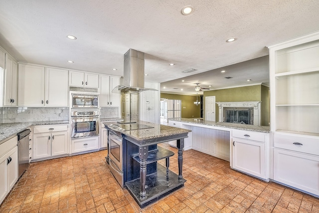 kitchen featuring appliances with stainless steel finishes, white cabinetry, light stone countertops, island exhaust hood, and decorative backsplash