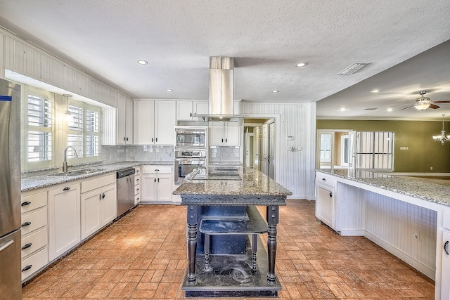 kitchen with appliances with stainless steel finishes, island range hood, sink, white cabinets, and light stone countertops