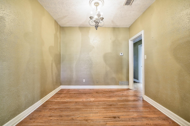 unfurnished dining area with an inviting chandelier, wood-type flooring, and a textured ceiling