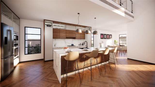 kitchen featuring decorative light fixtures, a center island with sink, light countertops, appliances with stainless steel finishes, and modern cabinets