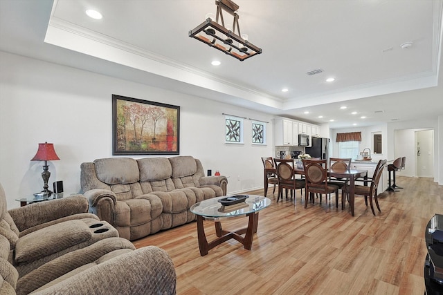 living room with a tray ceiling, light hardwood / wood-style flooring, and ornamental molding