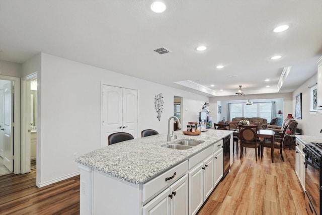 kitchen with white cabinets, an island with sink, sink, ceiling fan, and a tray ceiling