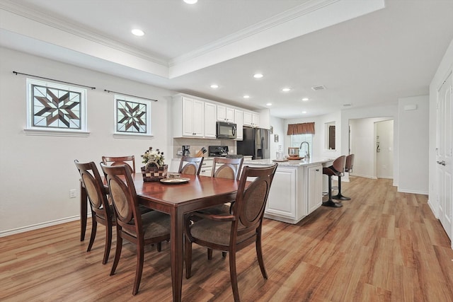 dining room with ornamental molding, a raised ceiling, sink, and light hardwood / wood-style flooring