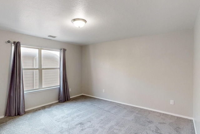 spare room featuring light colored carpet and a textured ceiling