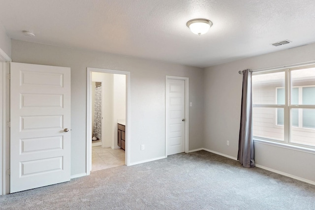 unfurnished bedroom featuring light carpet, connected bathroom, and a textured ceiling