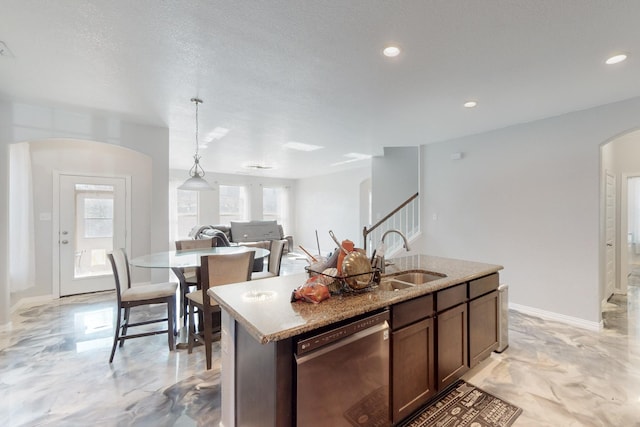 kitchen with pendant lighting, dishwasher, an island with sink, sink, and dark brown cabinetry