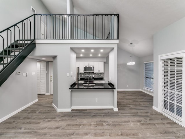 interior space featuring appliances with stainless steel finishes, white cabinetry, hanging light fixtures, sink, and high vaulted ceiling