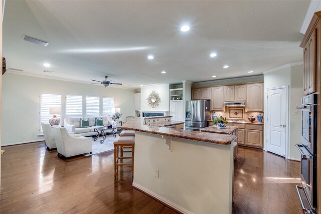 kitchen with appliances with stainless steel finishes, a breakfast bar, light brown cabinetry, an island with sink, and crown molding