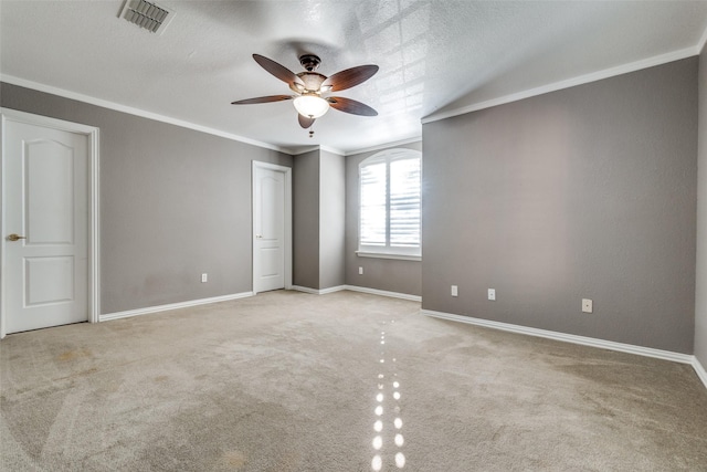 empty room featuring ceiling fan, light colored carpet, ornamental molding, and a textured ceiling