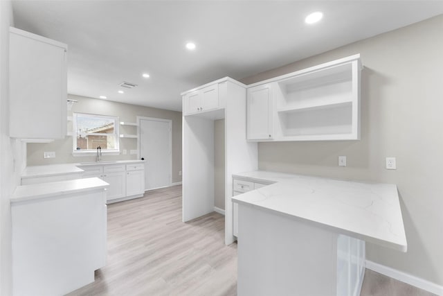 kitchen featuring white cabinets, sink, kitchen peninsula, light wood-type flooring, and light stone counters