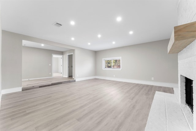 unfurnished living room featuring light wood-type flooring and a brick fireplace