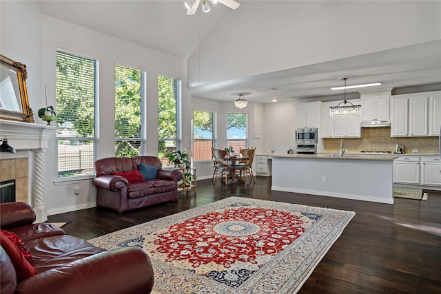 living room with dark wood-type flooring, sink, high vaulted ceiling, a tile fireplace, and ceiling fan