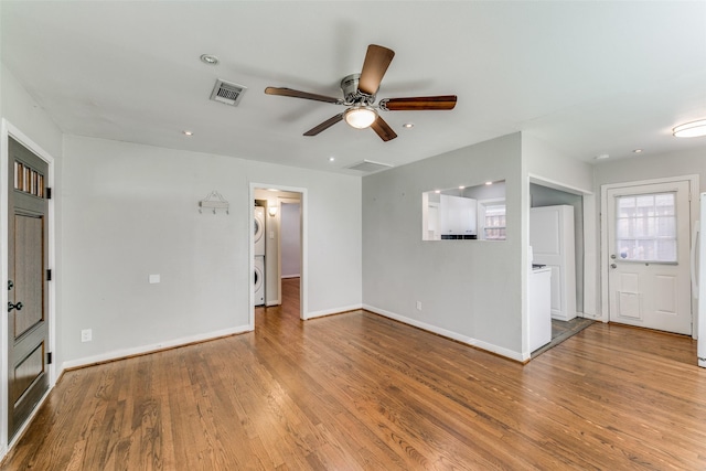 unfurnished living room featuring ceiling fan, stacked washer and dryer, and light hardwood / wood-style floors