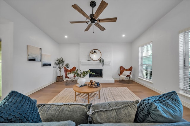 living room featuring vaulted ceiling, a brick fireplace, and wood finished floors