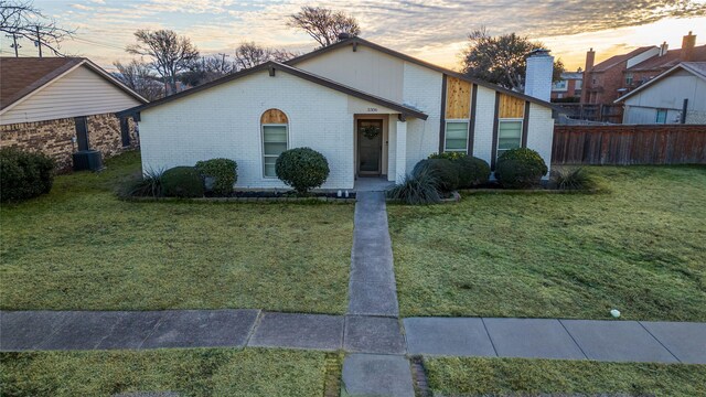 view of front of property with brick siding, a lawn, central AC unit, and fence