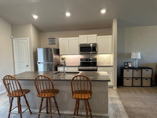 kitchen with a center island with sink, appliances with stainless steel finishes, dark stone countertops, and white cabinetry