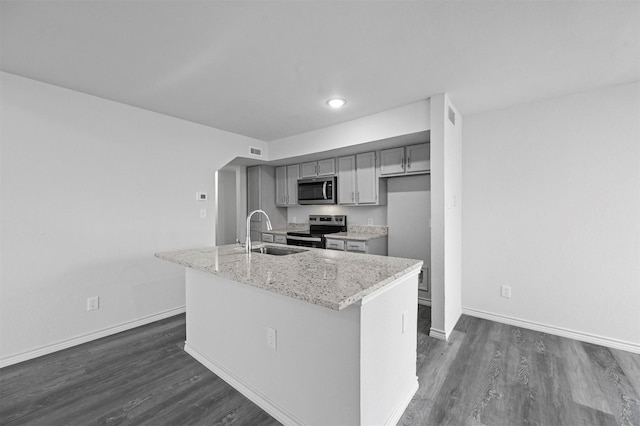 kitchen with gray cabinets, a center island with sink, sink, appliances with stainless steel finishes, and light stone counters