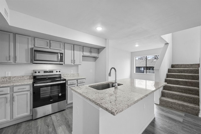 kitchen with light stone countertops, stainless steel appliances, sink, dark hardwood / wood-style floors, and a center island with sink