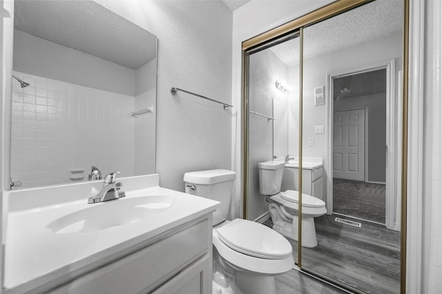 bathroom featuring wood-type flooring, toilet, vanity, and a textured ceiling