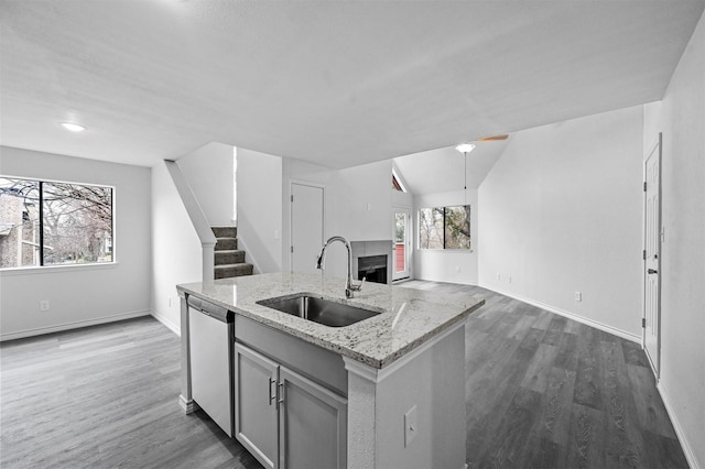 kitchen featuring lofted ceiling, gray cabinets, stainless steel dishwasher, sink, and light stone countertops