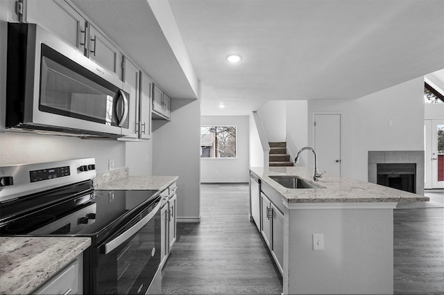 kitchen featuring a fireplace, a center island with sink, sink, appliances with stainless steel finishes, and light stone counters