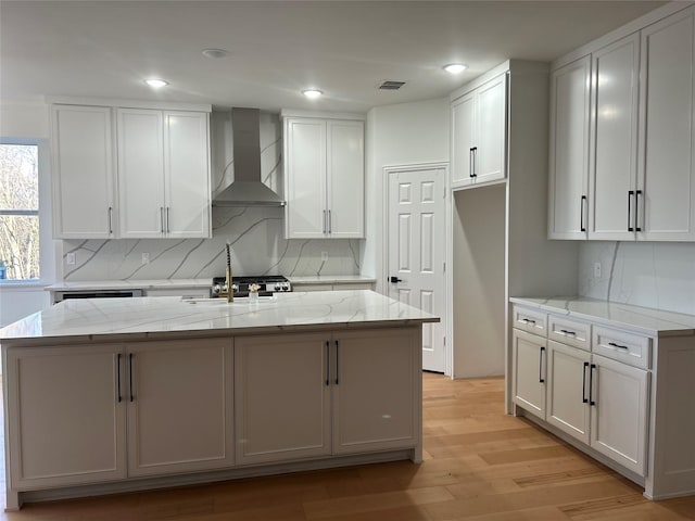 kitchen with white cabinetry, wall chimney exhaust hood, and a kitchen island with sink