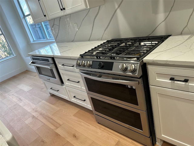 kitchen featuring tasteful backsplash, white cabinets, light stone countertops, and stainless steel appliances