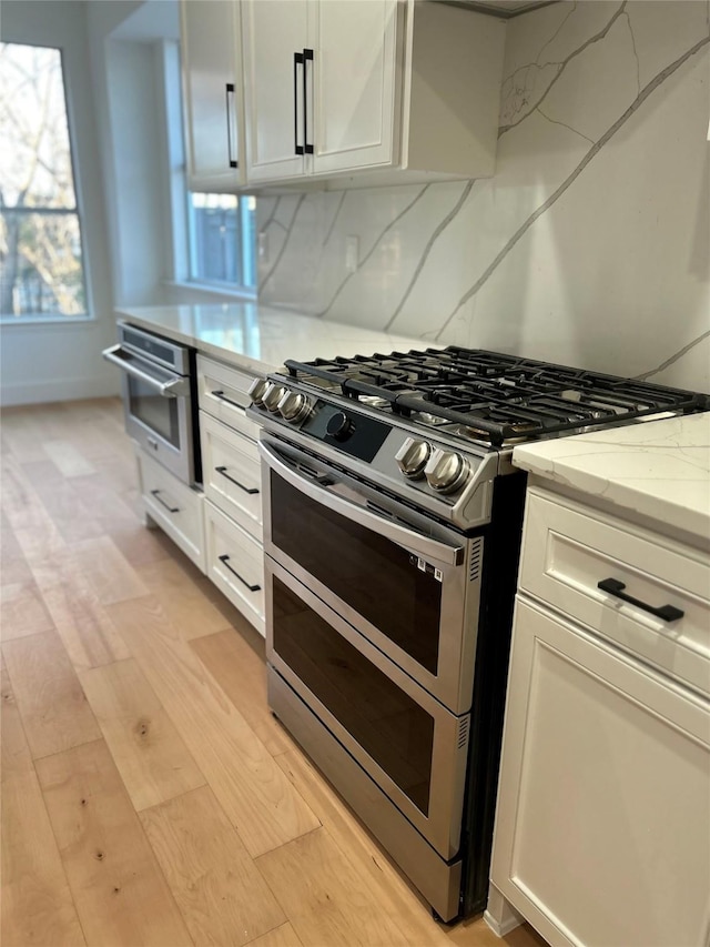 kitchen featuring light stone countertops, white cabinetry, range with two ovens, decorative backsplash, and light wood-type flooring